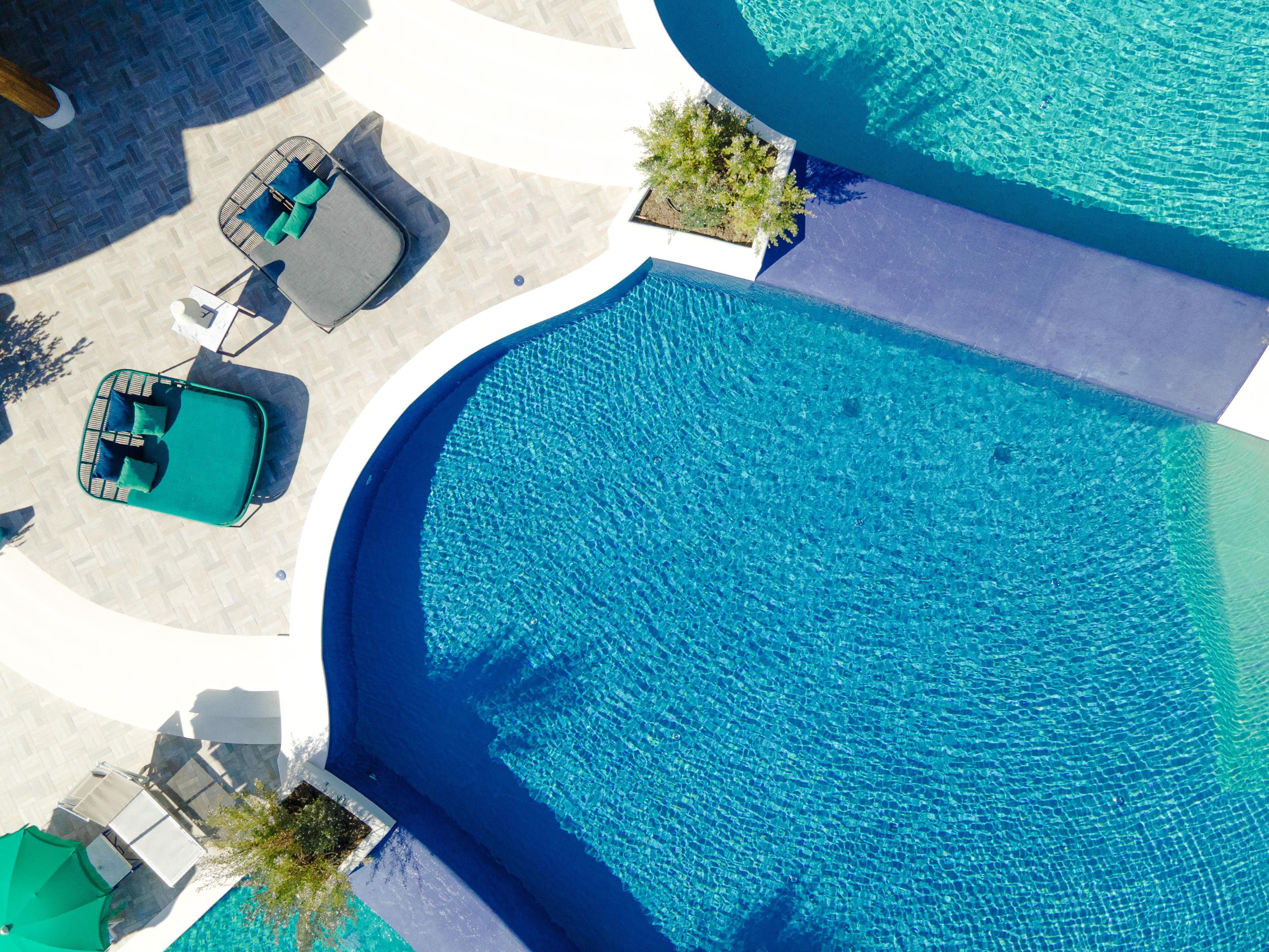 Vista aérea de uma área de piscina com espreguiçadeiras e uma mesa pequena.
