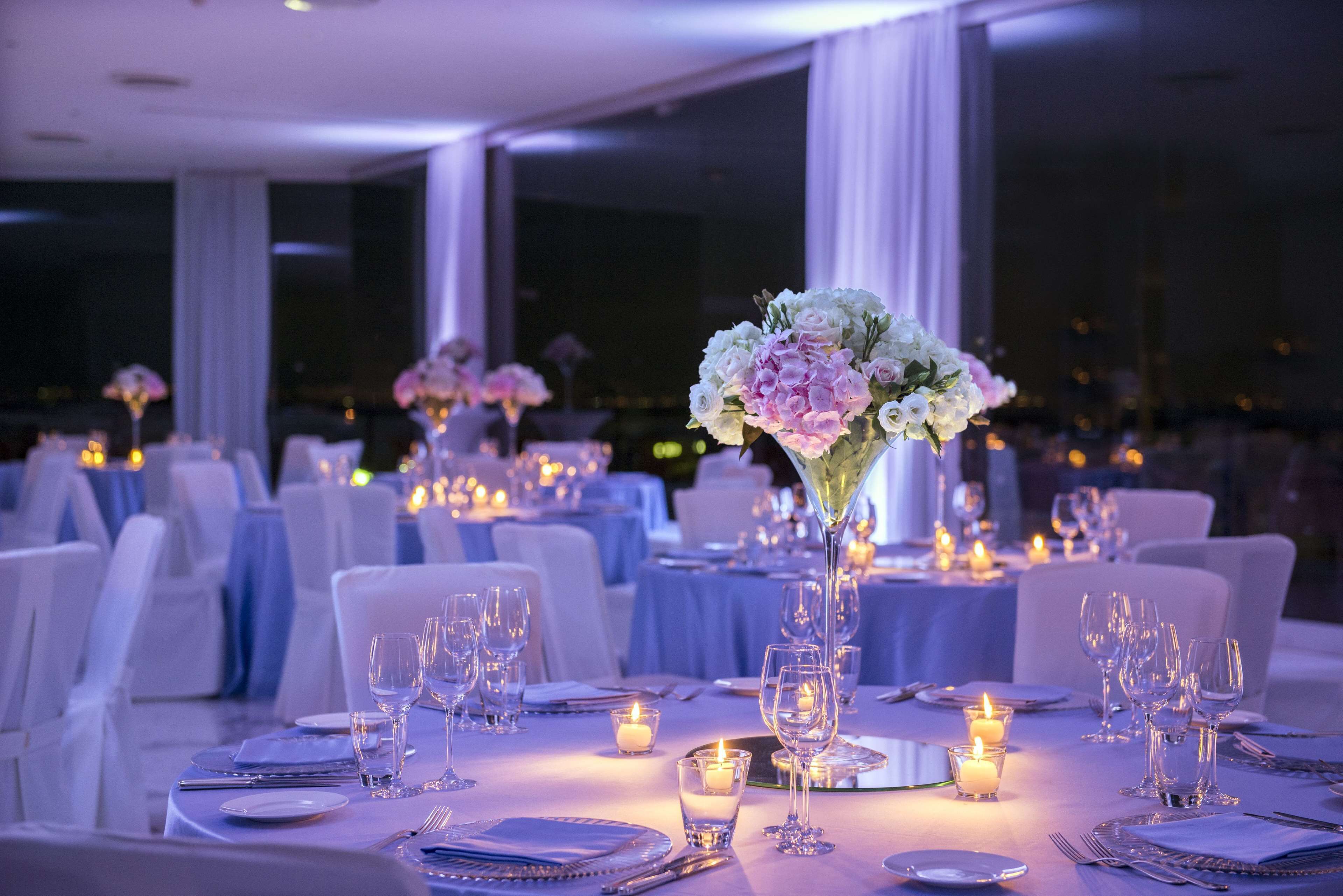 A formal dining setup with tables set for a meal, candles, and floral centerpieces.