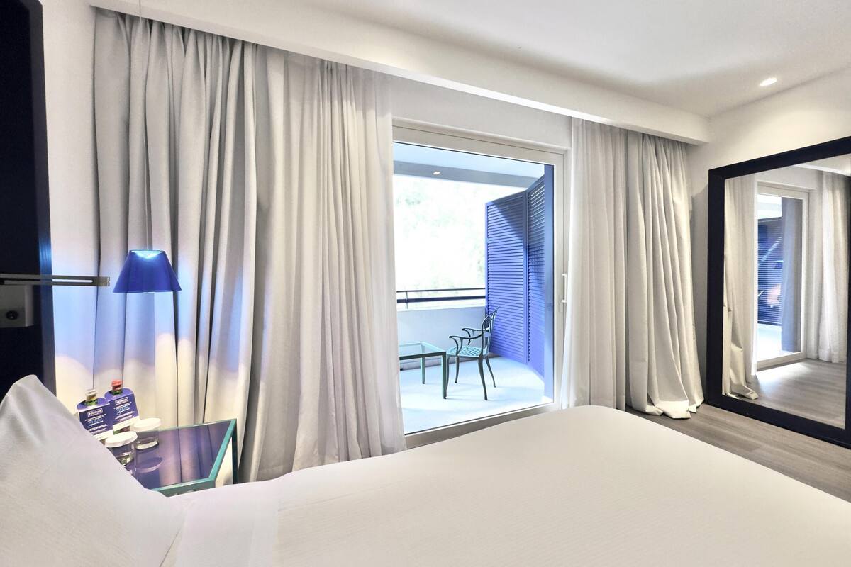 Une chambre d’hôtel avec un grand lit, un bureau avec une lampe, une chaise et un balcon avec vue.