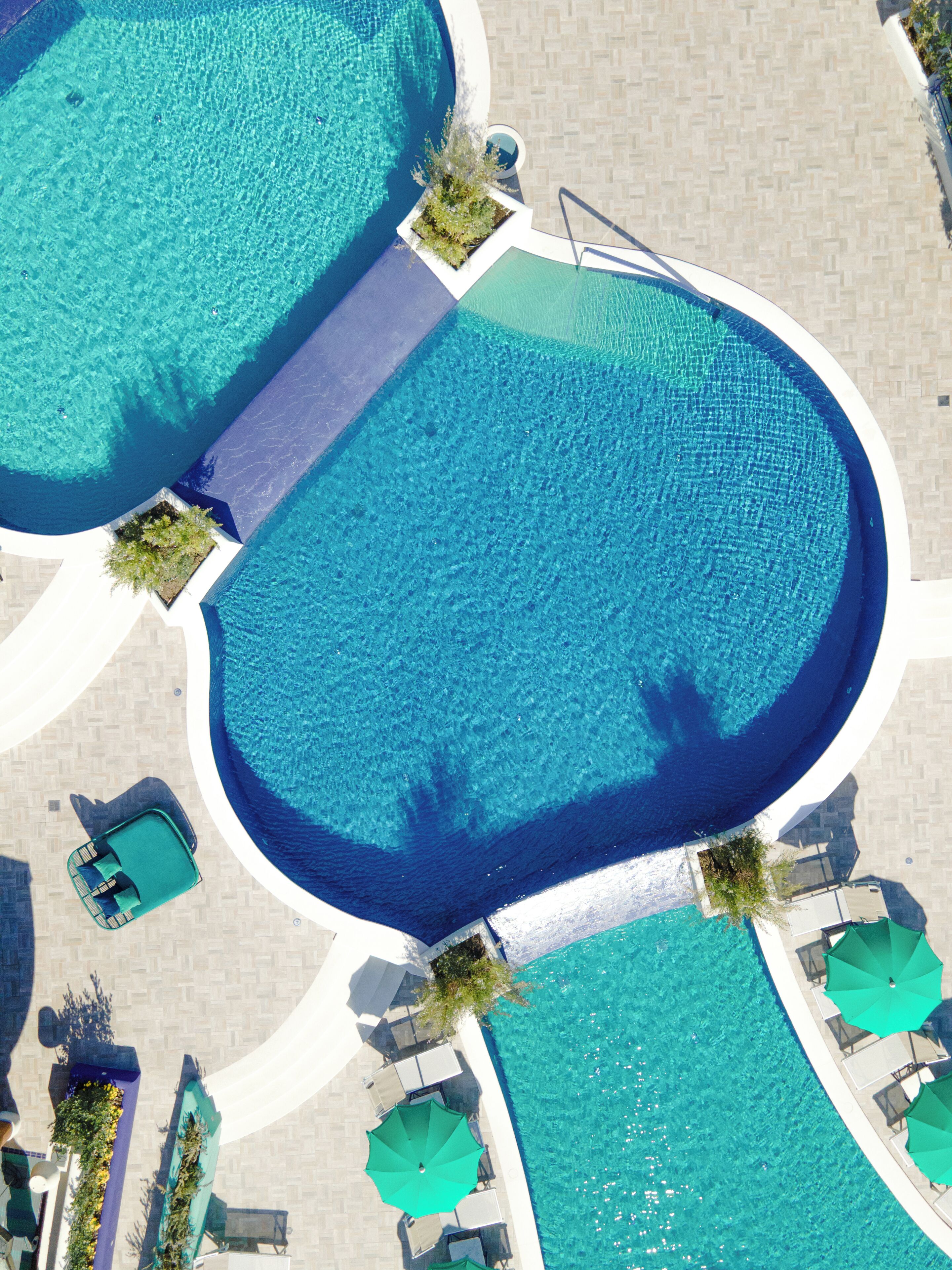 Vista aérea de un hotel con dos piscinas grandes, una zona de estar techada y un pequeño muelle para embarcaciones.