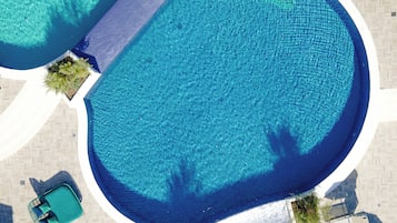 An aerial view of a hotel with two large swimming pools, a covered seating area, and a small boat dock.