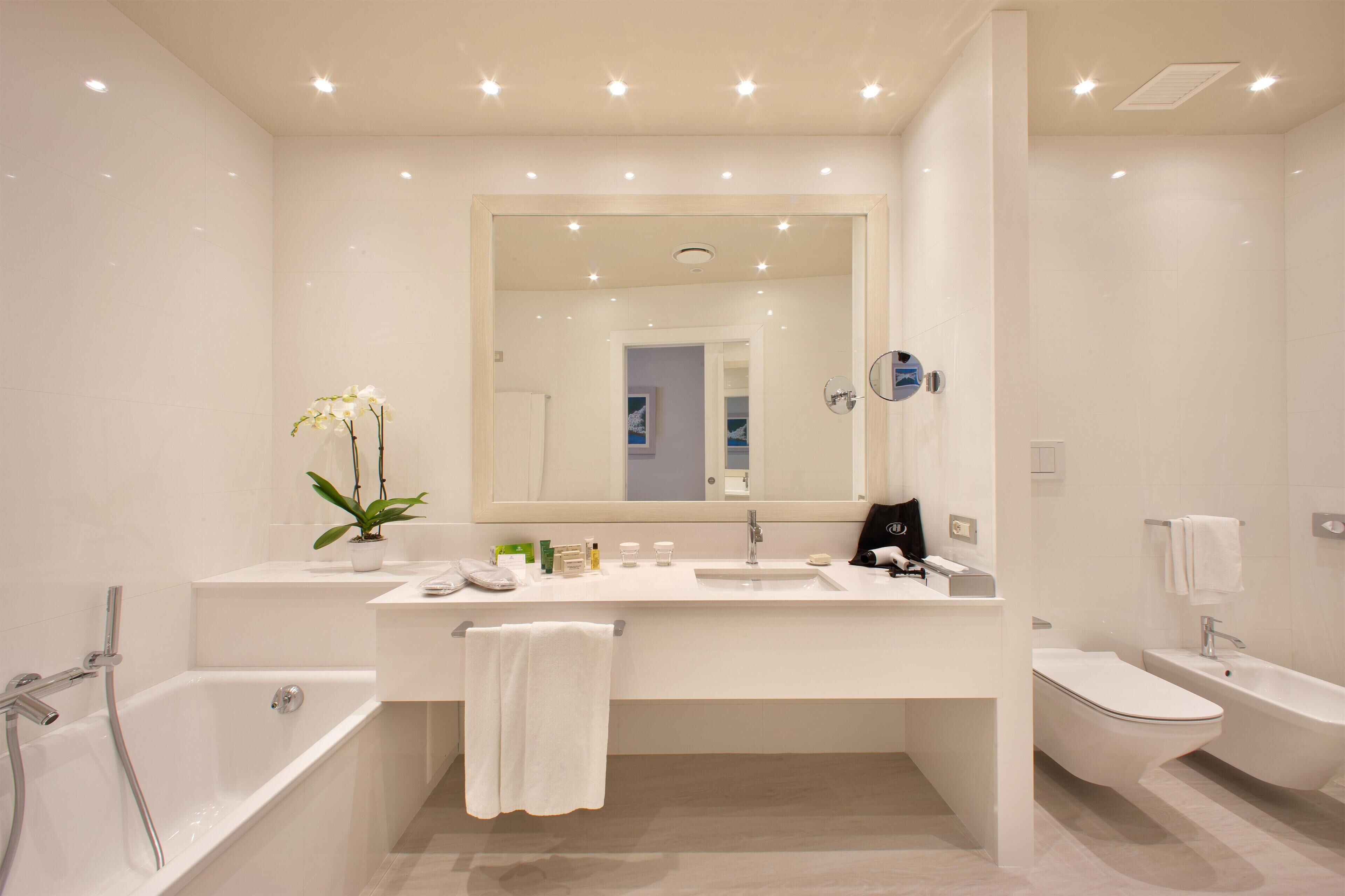 A modern bathroom with a bathtub, a sink, a mirror, and a toilet.