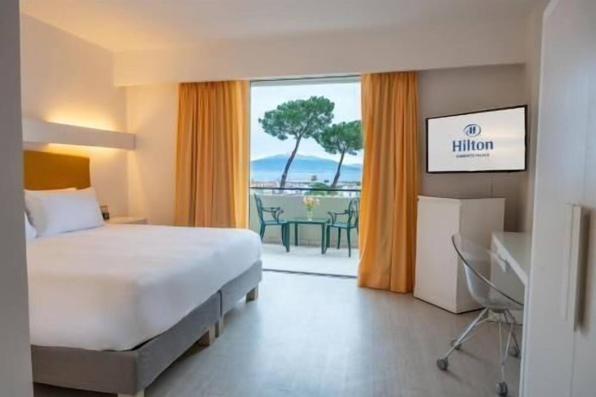 Une chambre d’hôtel avec un lit, un bureau, une chaise et un balcon offrant une vue.