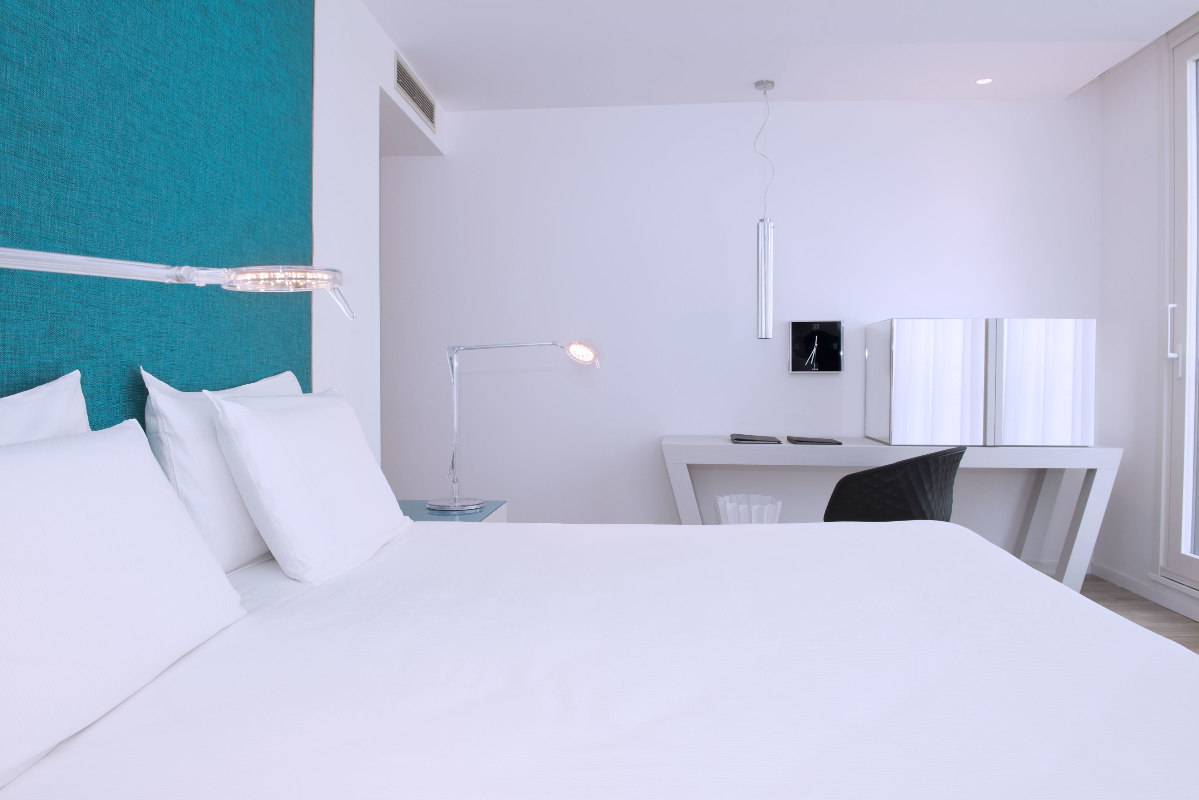 A modern hotel room with a large bed, a desk, and a chair.