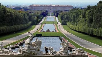 A grand palace with symmetrical gardens, a central water feature, and statues.
