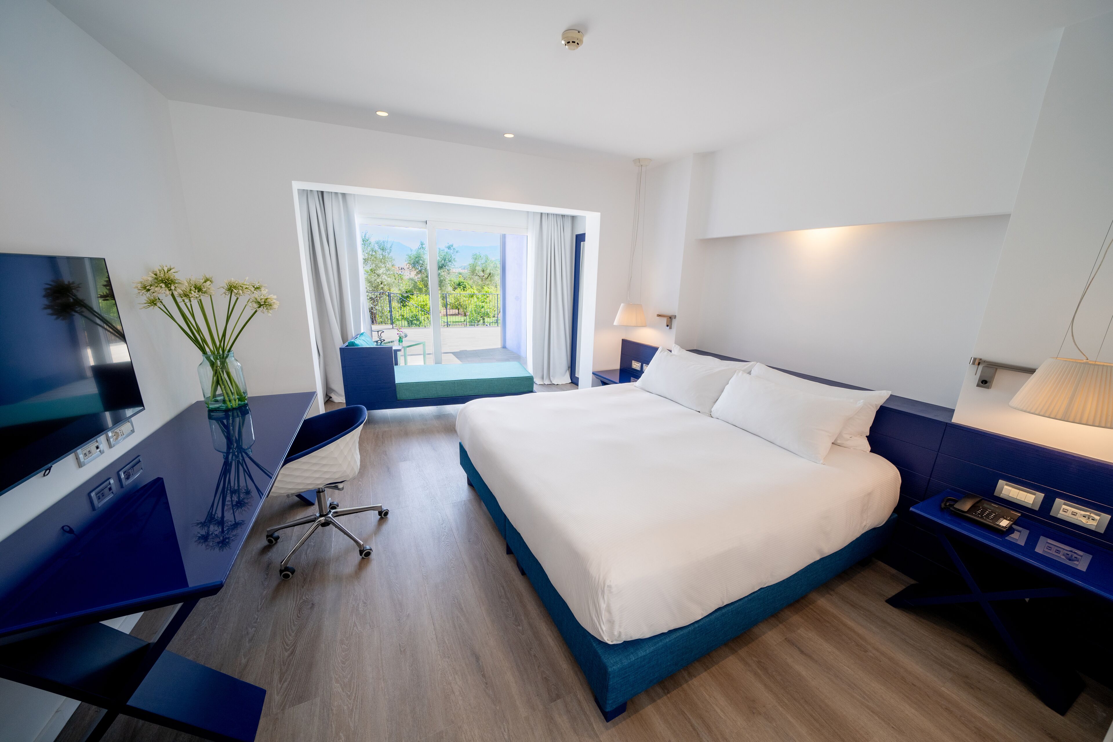 Una habitación de hotel moderna con una cama grande, un escritorio con ordenador y vistas al exterior.