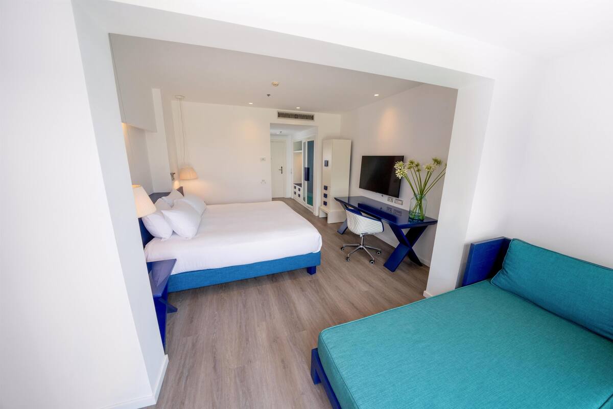 Une chambre d’hôtel équipée d’un lit, d’un bureau, d’une chaise, d’une télévision et d’un vase avec des fleurs.