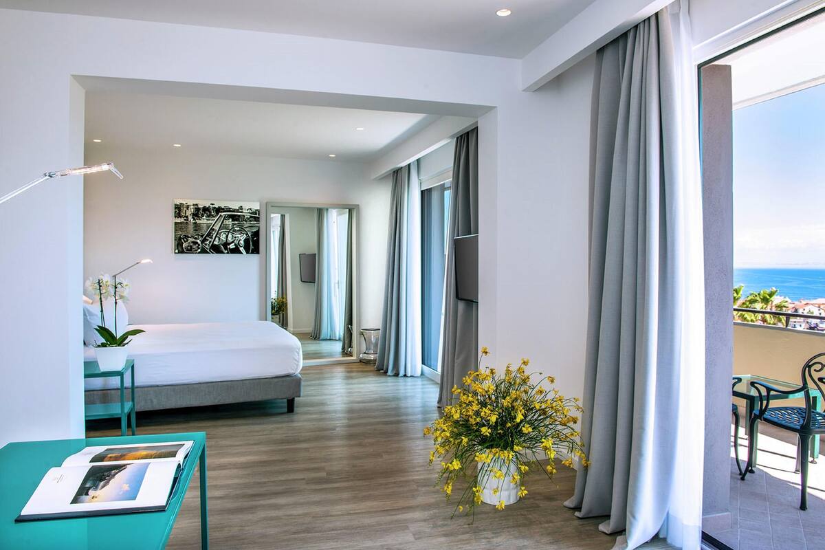 Une chambre d’hôtel moderne, équipée d’un lit, d’un bureau, d’une chaise, d’une plante en pot et offrant une vue sur l’océan.
