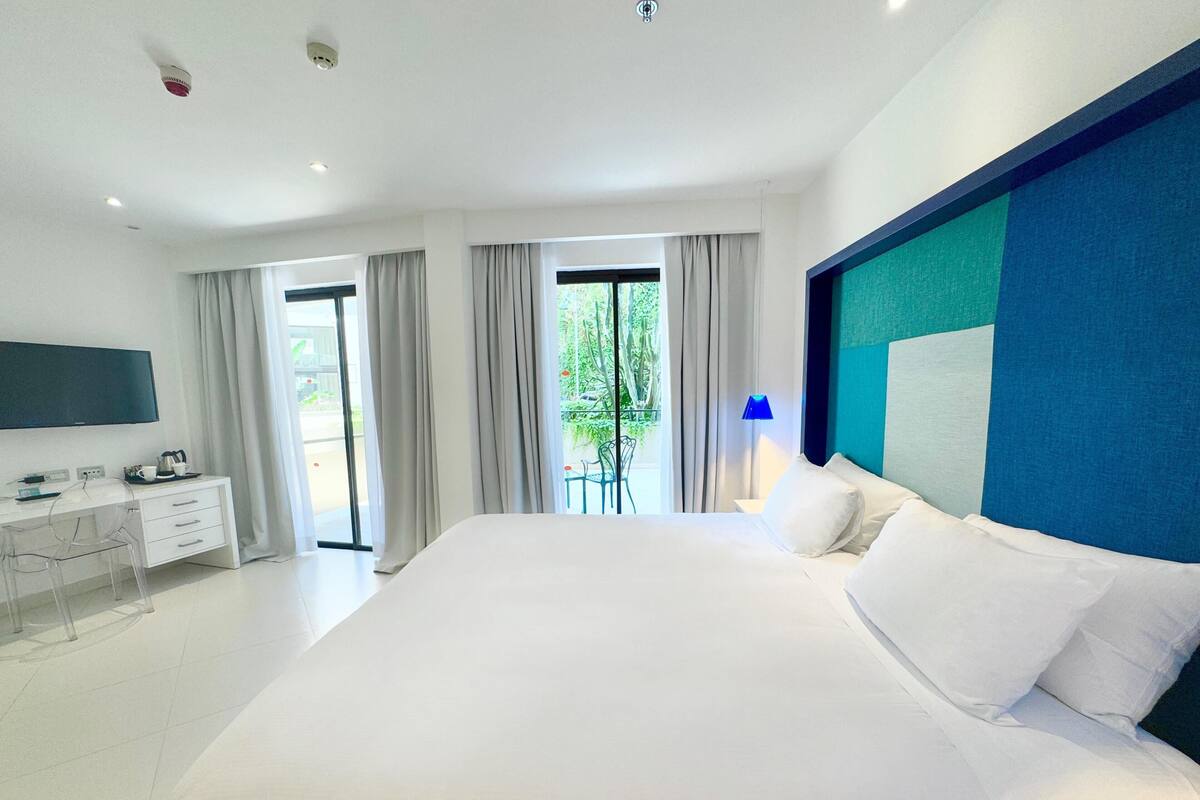 Une chambre d’hôtel moderne dotée d’un grand lit, d’un bureau avec un téléviseur à écran plat et d’un balcon avec des rideaux.