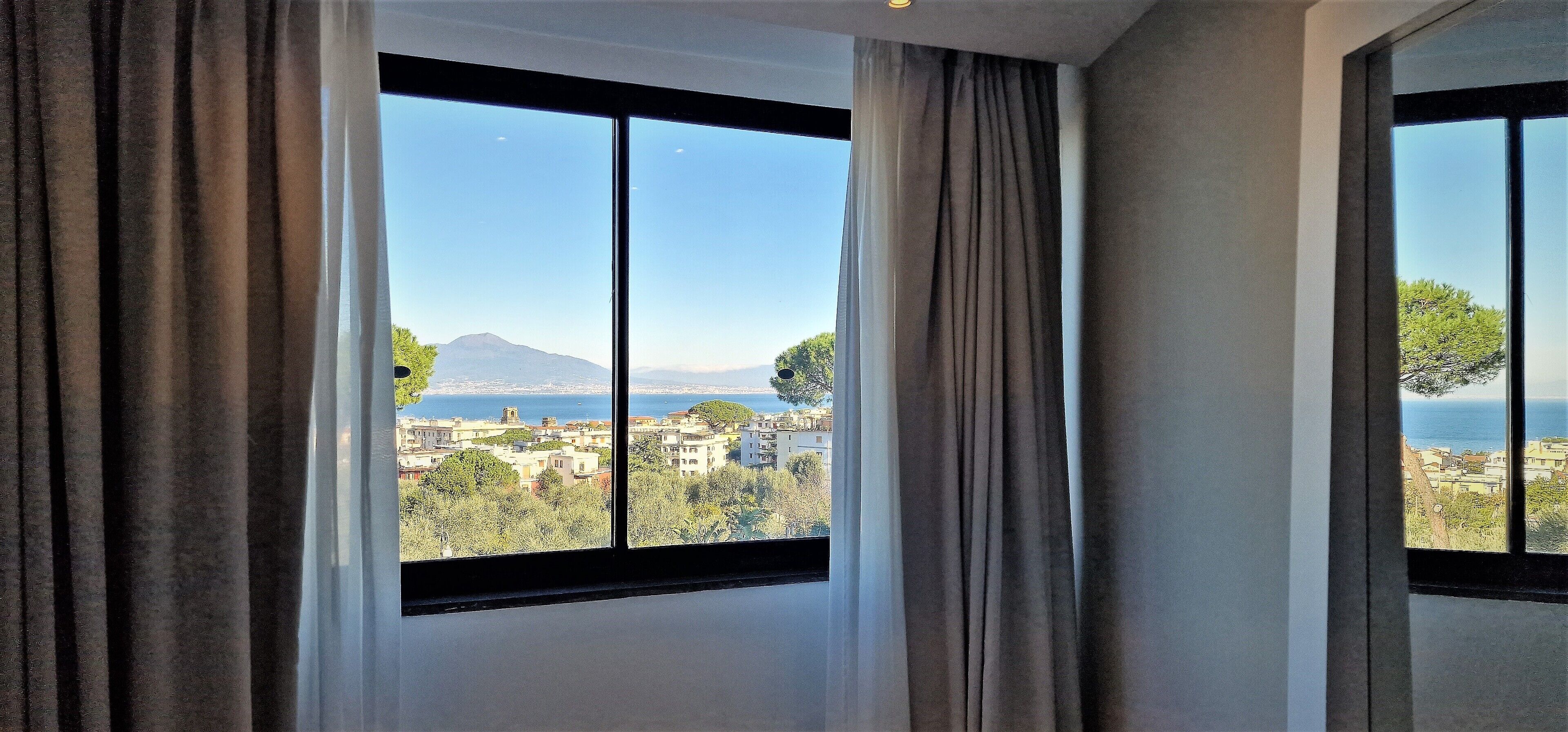 A room with large windows offering a view of a cityscape, mountains, and a body of water.