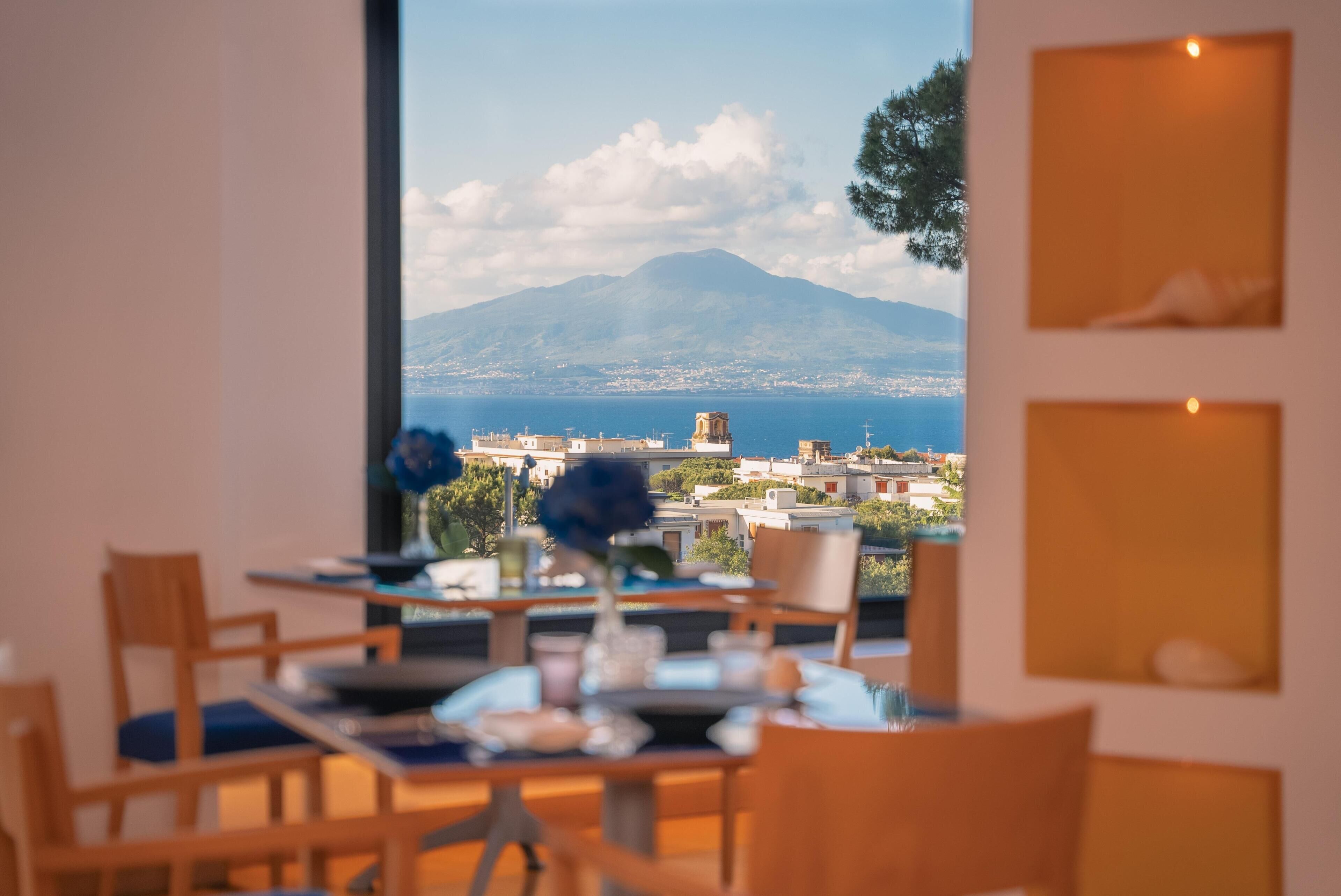 Un comedor con una mesa y sillas, un florero con flores y vistas a un paisaje urbano con una montaña al fondo.