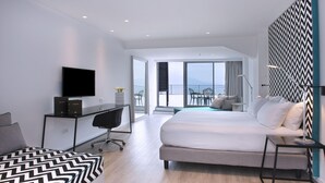 Ein modernes Hotelzimmer mit einem großen Bett, einem Schreibtisch mit Computer, einem Fernseher und einem Balkon mit Blick.