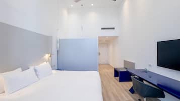 A modern hotel room with a bed, desk, chair, ceiling fan, and TV.