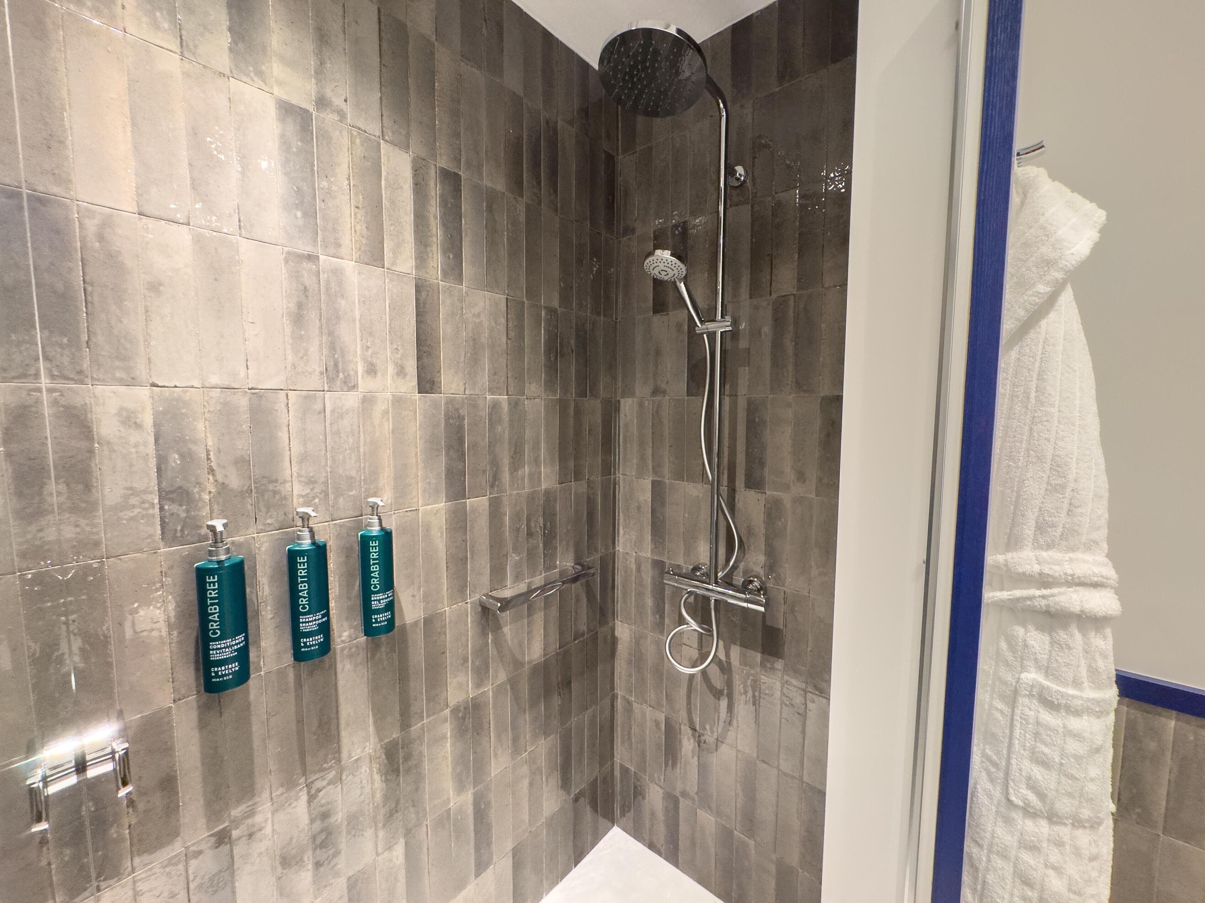 A shower with a rain showerhead, a handheld showerhead, and a handheld scrubber.