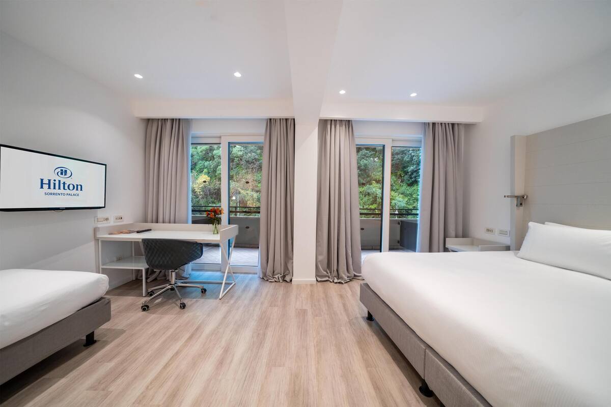 Une chambre d’hôtel moderne équipée d’un lit, d’un bureau, d’une chaise et de grandes fenêtres.