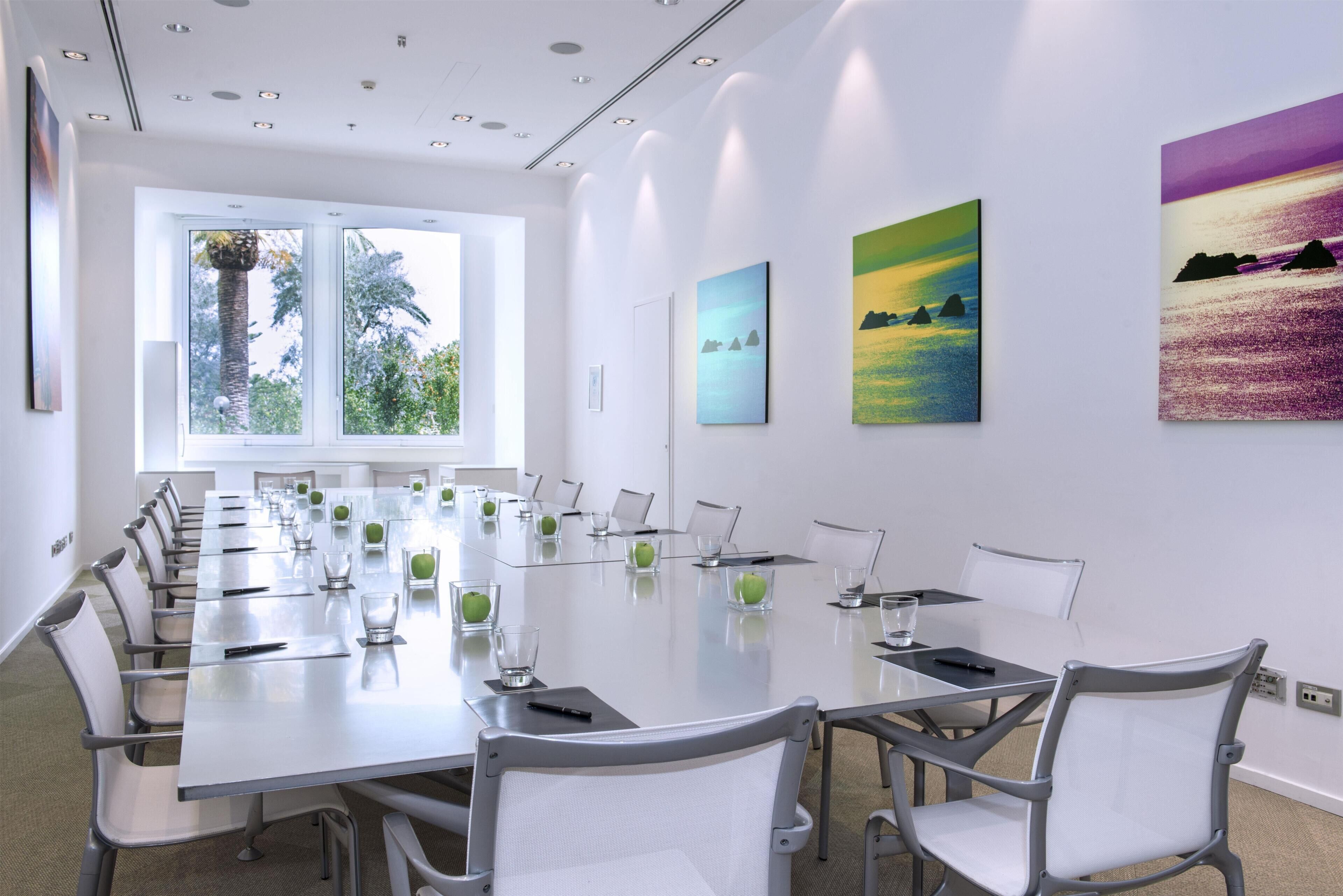 A conference room with a long table, white chairs, and artwork on the walls.