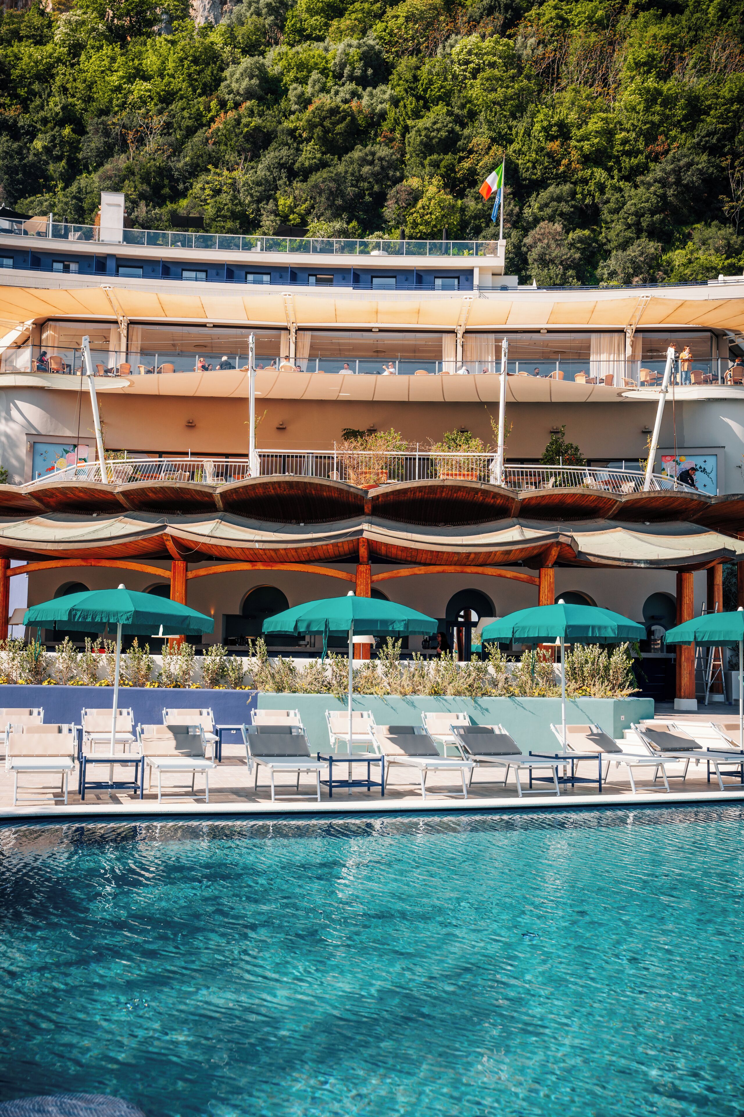 A hotel with a pool area, lounge chairs, and umbrellas.