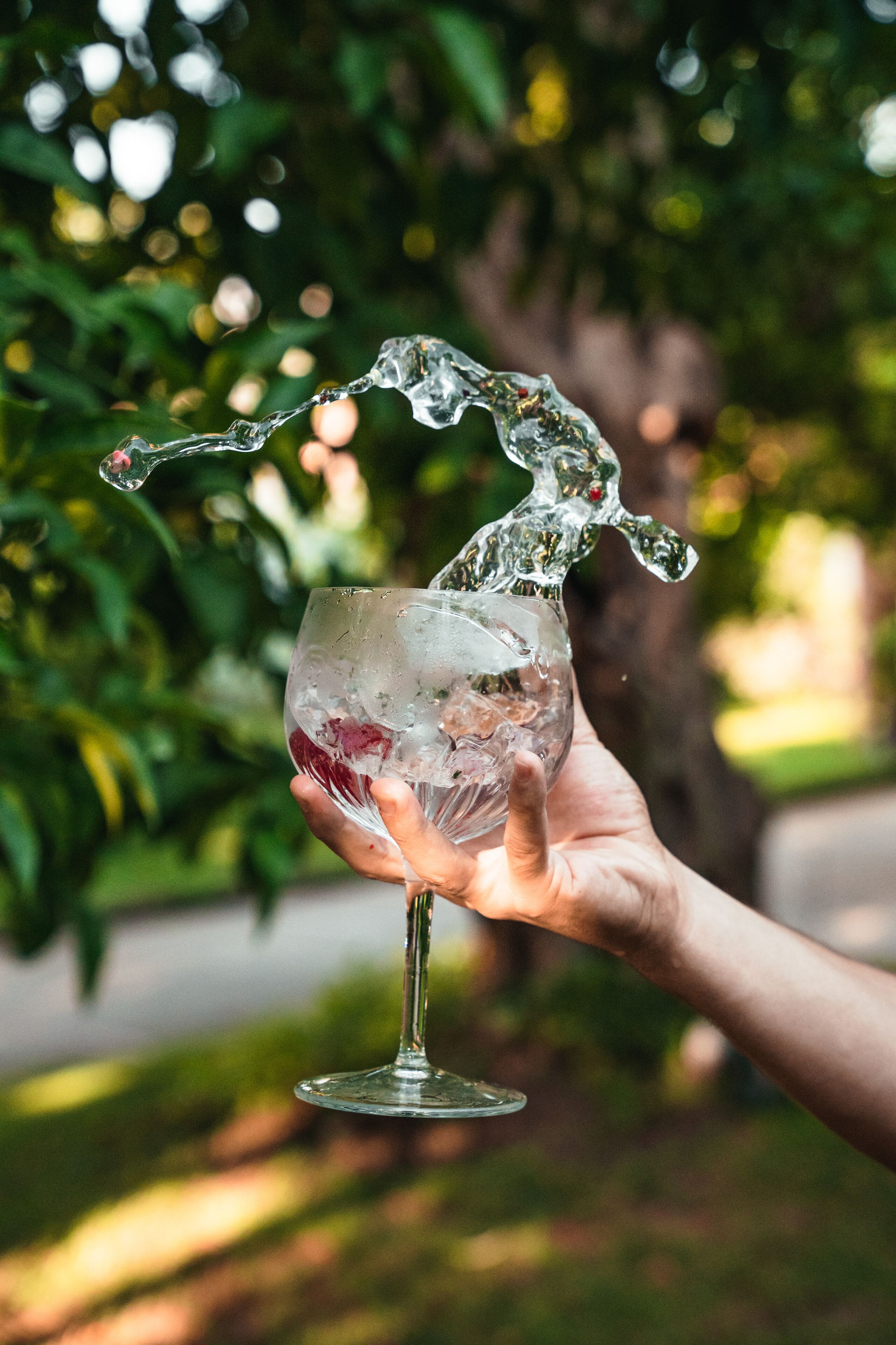 Eine Hand hält ein Glas mit einer klaren Flüssigkeit und Eiswürfeln.