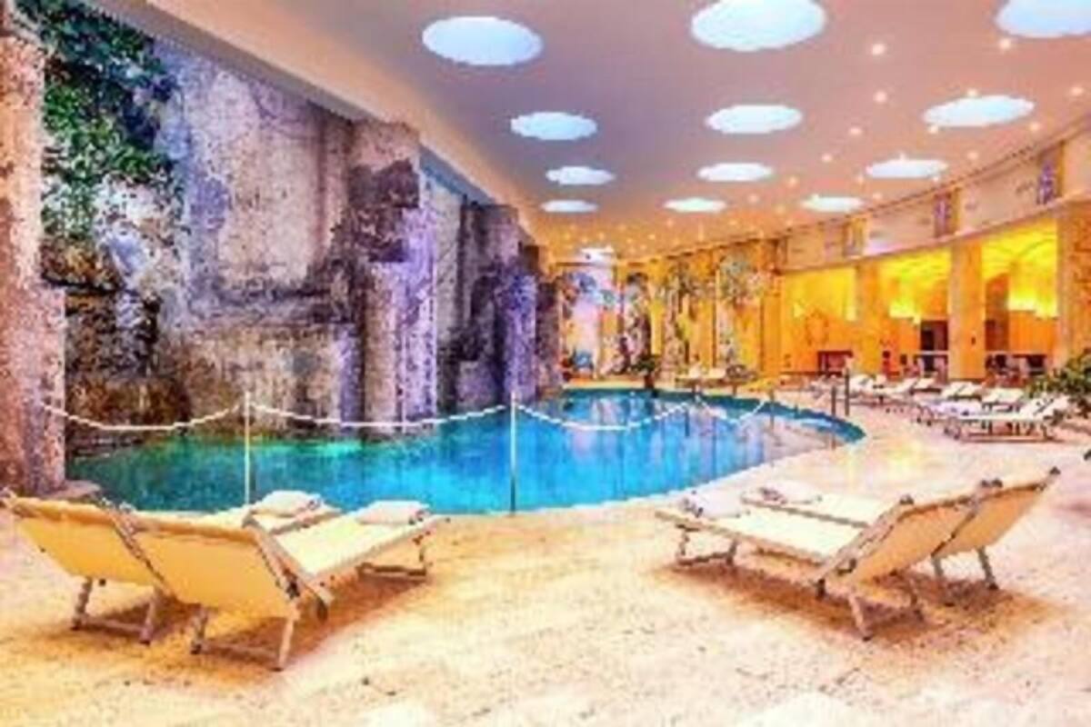 Une piscine intérieure dotée de chaises longues, d’un mur d’escalade et d’un plafond orné de luminaires circulaires.