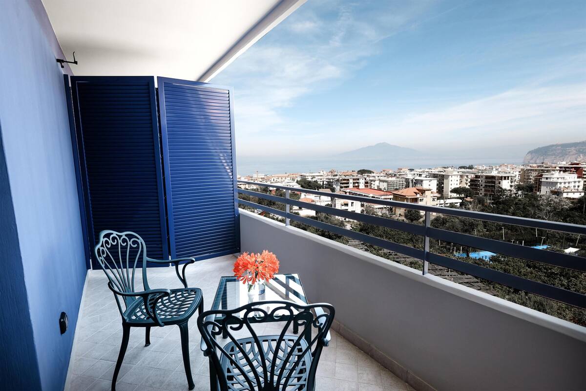 Un balcon avec deux chaises, une table et un vase de fleurs.
