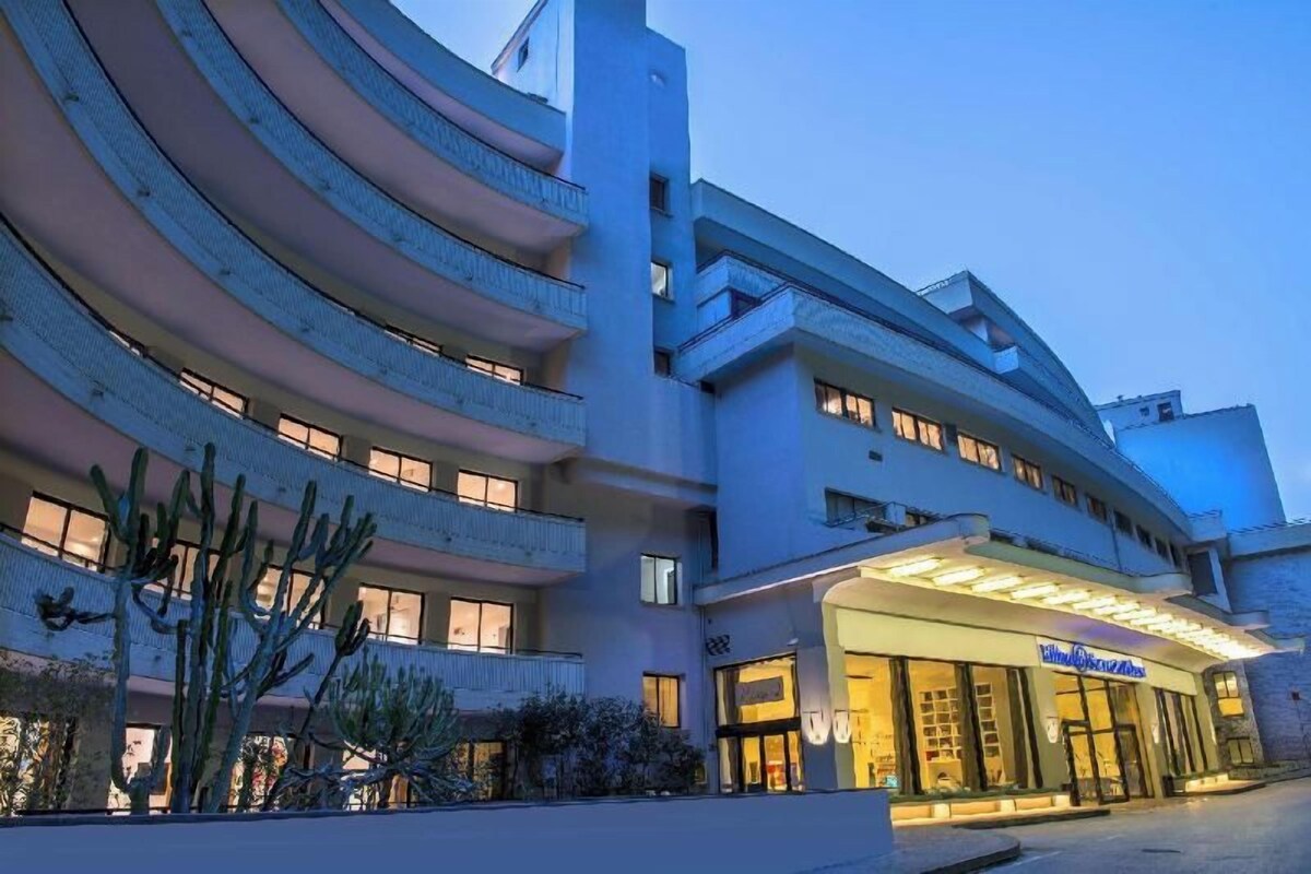 Un hotel a più piani con facciata curva, balconi e un ingresso ben illuminato.