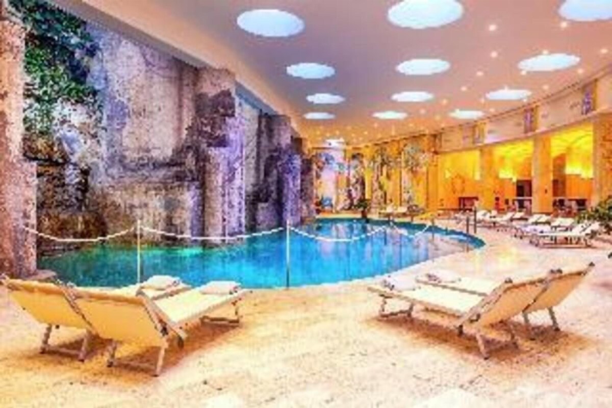 Une piscine intérieure dotée de chaises longues, d’un mur d’escalade et d’un plafond orné de luminaires circulaires.