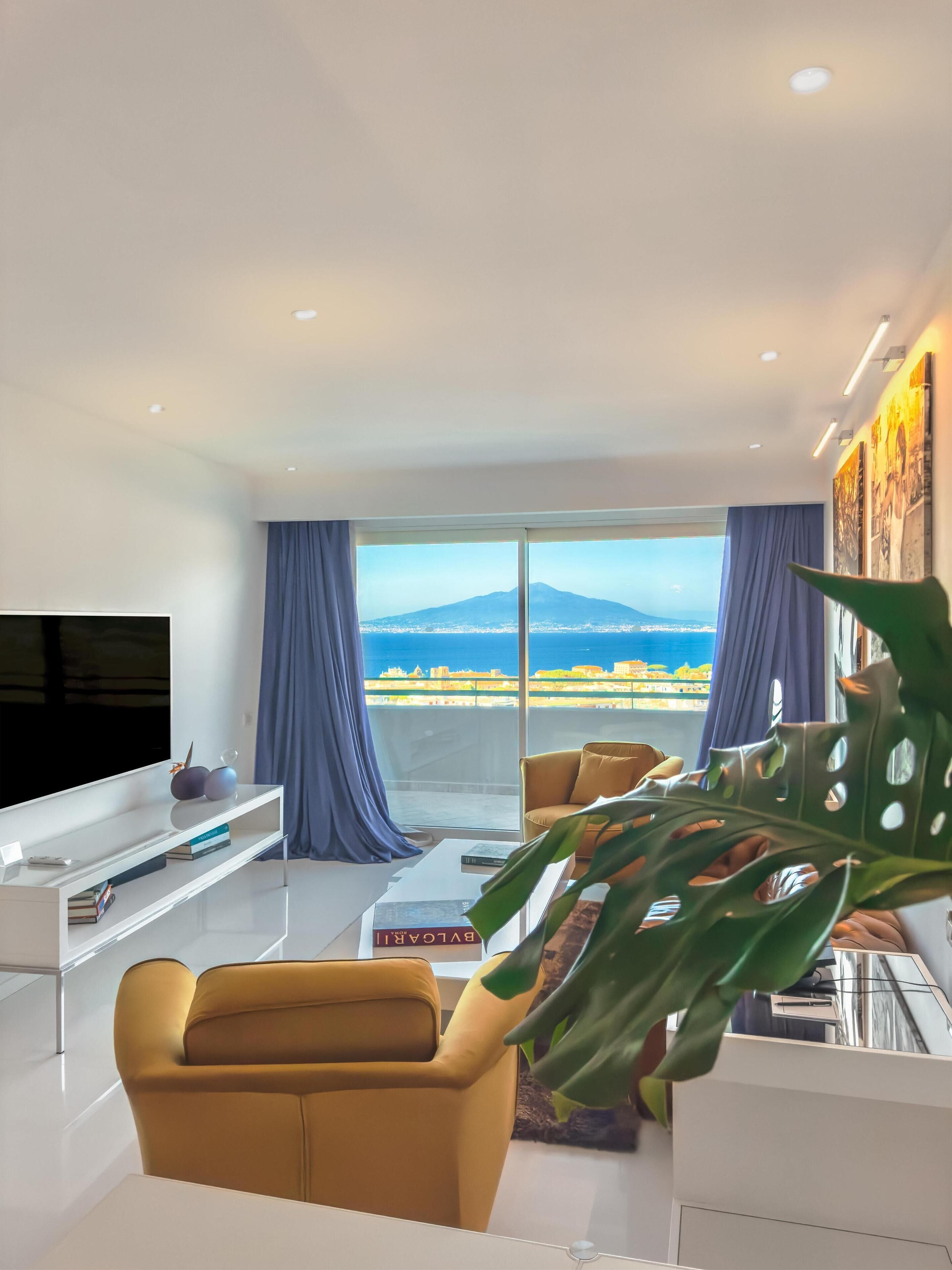 A modern living room with a sofa, a coffee table, a TV, and a large window with a view of a mountain and cityscape.
