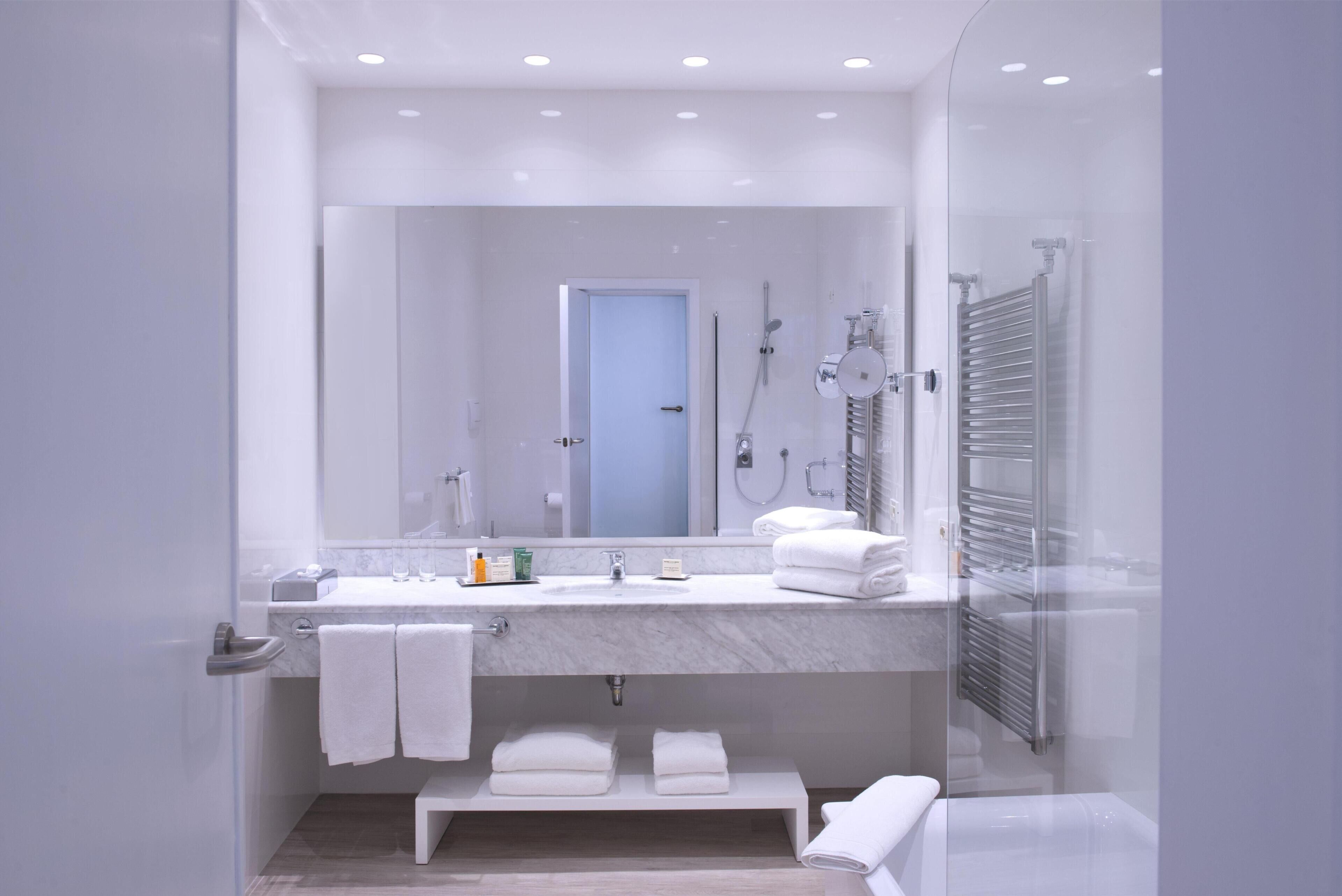 Un baño moderno con lavamanos de mármol, un espejo grande, ducha con mampara de vidrio y un perchero para toallas.