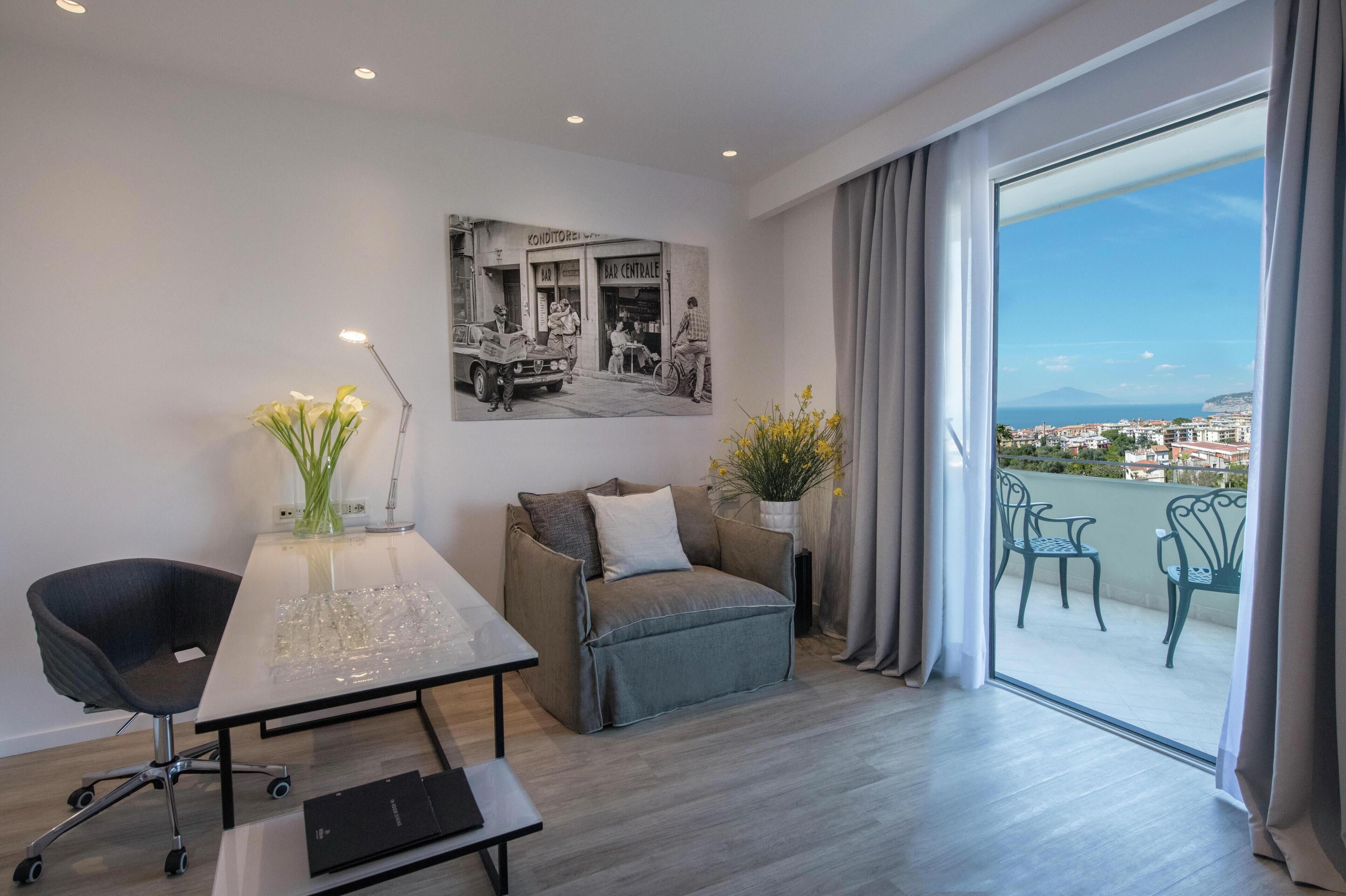 Una habitación moderna con una mesa de comedor, una silla de escritorio, un sofá y un amplio ventanal con vistas a un paisaje urbano.