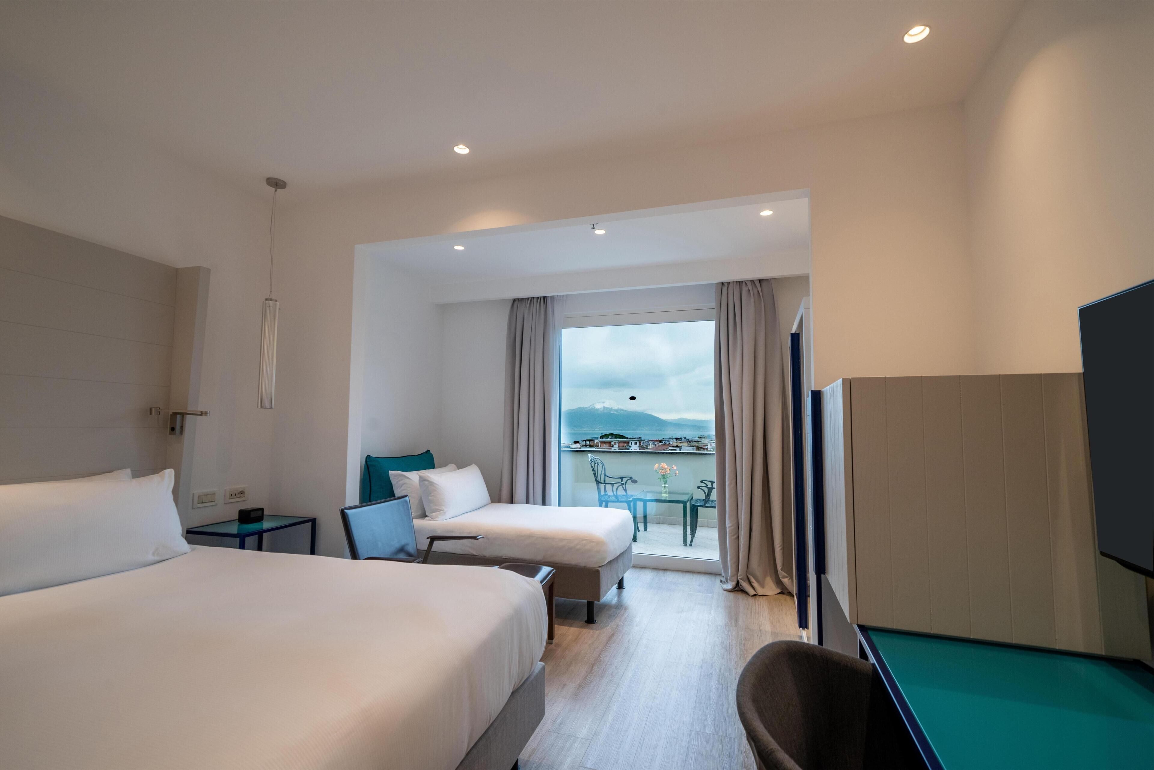A hotel room with two beds, a desk, a chair, a pool table, and a balcony with a view.