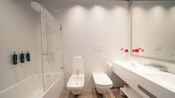 A modern bathroom with a glass-enclosed shower, a bidet, a toilet, and a vanity with a mirror.