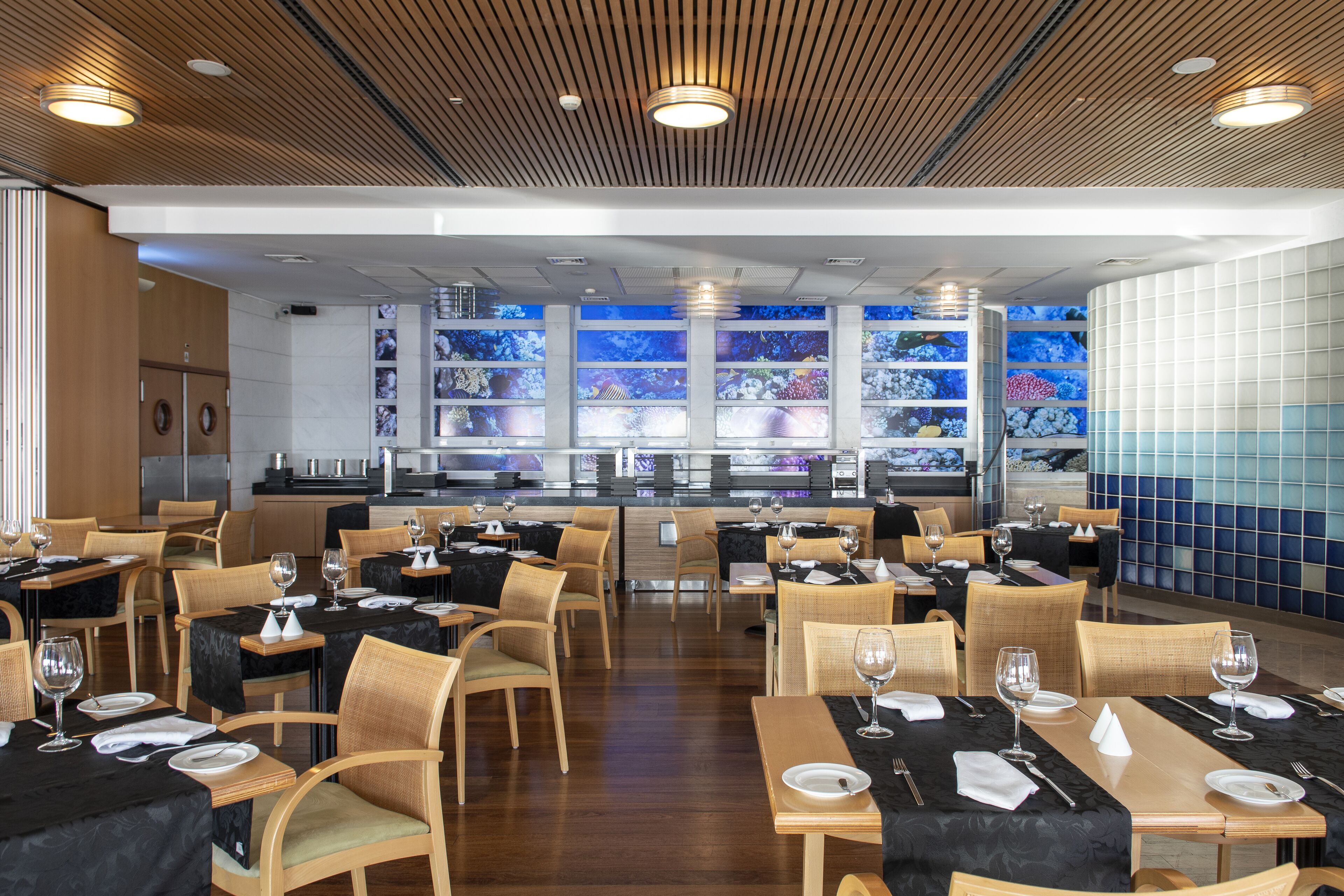 Un restaurante con techo de madera, manteles negros y acuarios de vidrio al fondo.