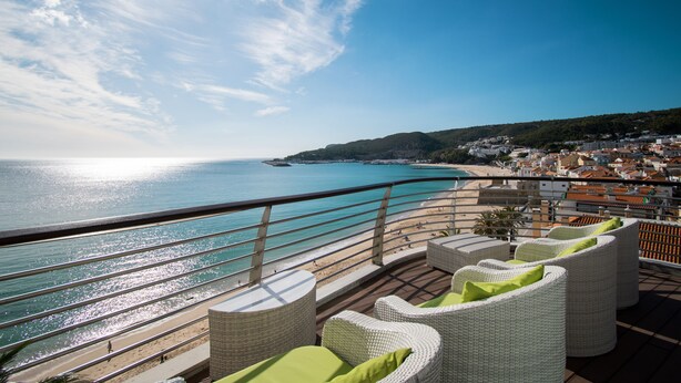 Una terraza frente al mar con muebles de mimbre y vistas a la playa y el océano.