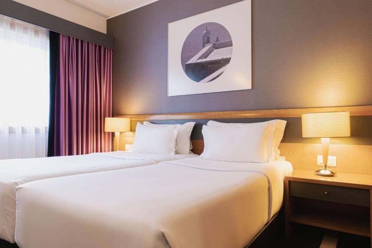 Une chambre d’hôtel avec deux lits, une table de chevet avec une lampe et un tableau encadré au mur.