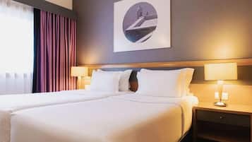 A hotel room with two beds, a nightstand with a lamp, and a framed picture on the wall.