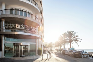 A hotel with a revolving door entrance, a sign reading 'SANA SESIMBA,' and a view of the ocean with palm trees. - SANA Sesimbra Hotel (Sesimbra)