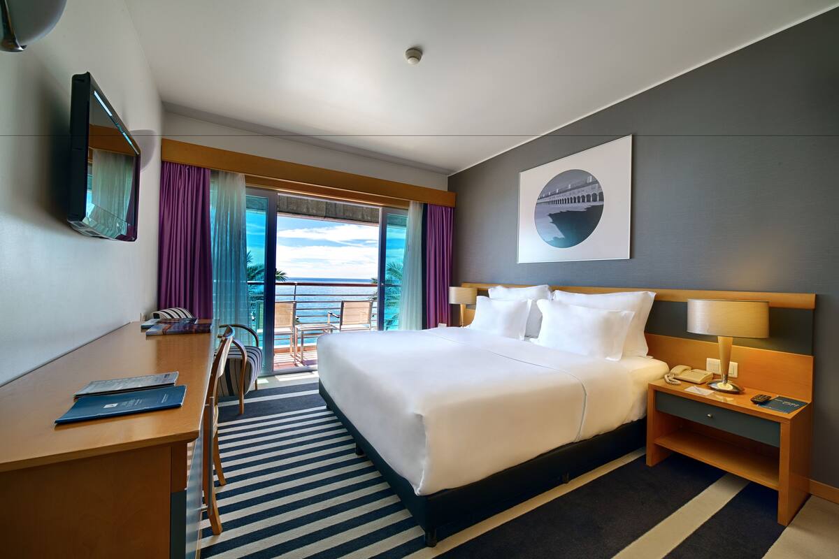 Une chambre d’hôtel avec un lit, une table de chevet, une lampe et une vue sur l’extérieur.
