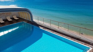 Una piscina con agua azul cristalina, una terraza con sillones de descanso y vista al océano.