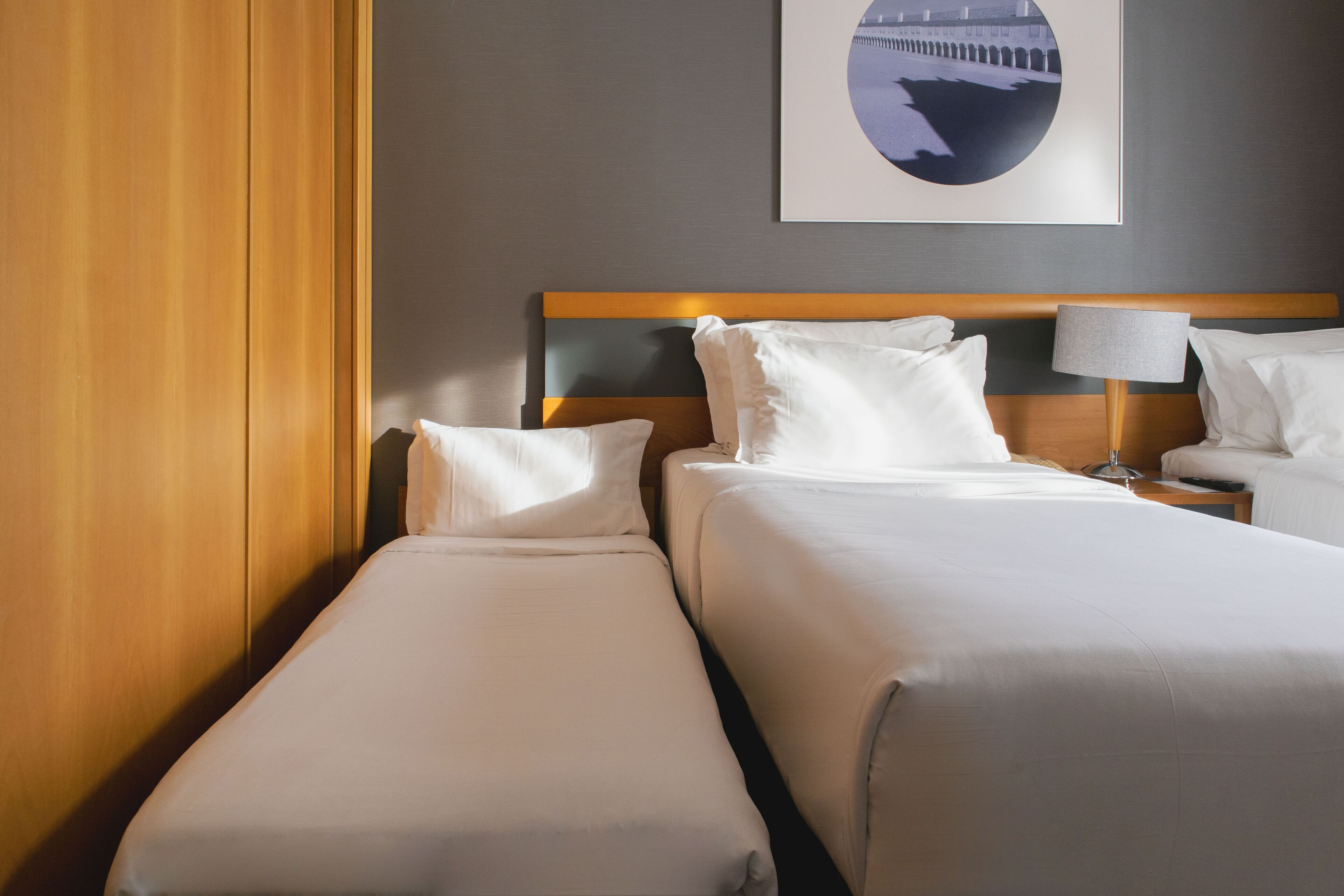 Een hotelkamer met twee bedden, een houten hoofdbord, een nachtkastje met een lamp en een ingelijste foto aan de muur.