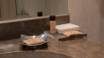 Una encimera de baño con una botella de leche corporal, un paquete de pañuelos y un dispensador de pañuelos.