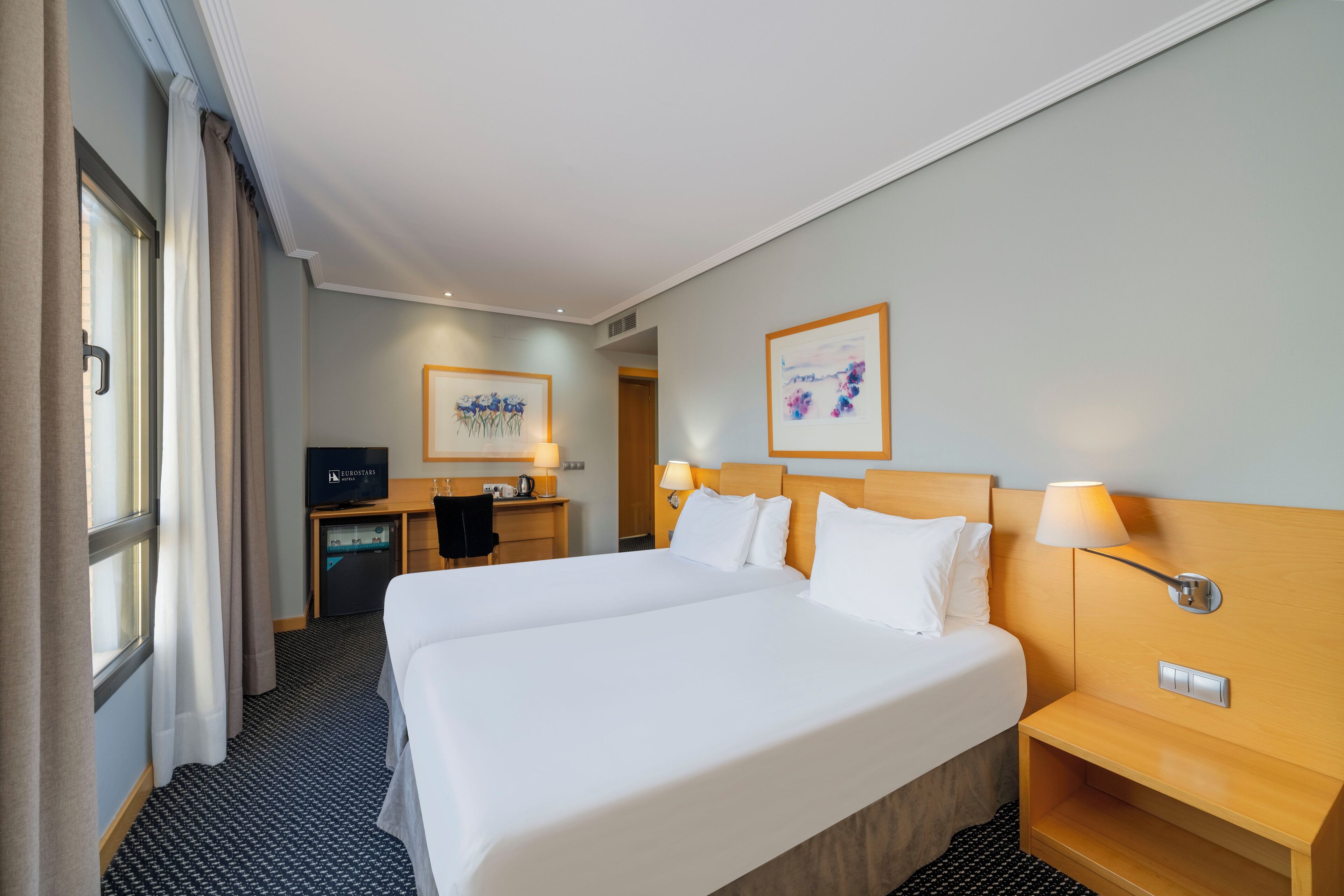 A hotel room with a large bed, a desk with a computer, and a TV.