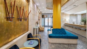 Un hall con un sofá azul, un pilar amarillo y una mesa de recepción.