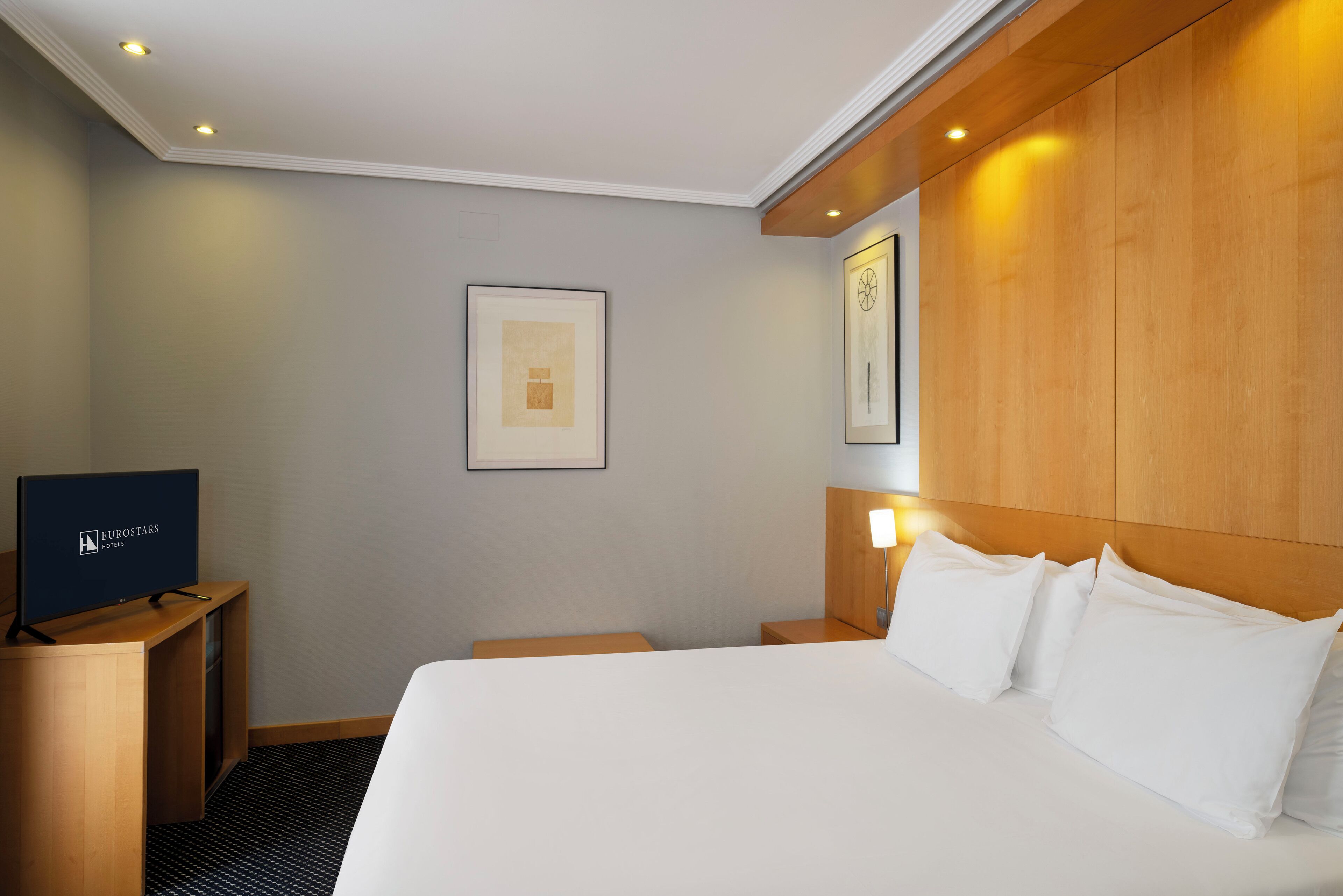 Habitación de hotel con cama, televisor y cuadros en la pared.