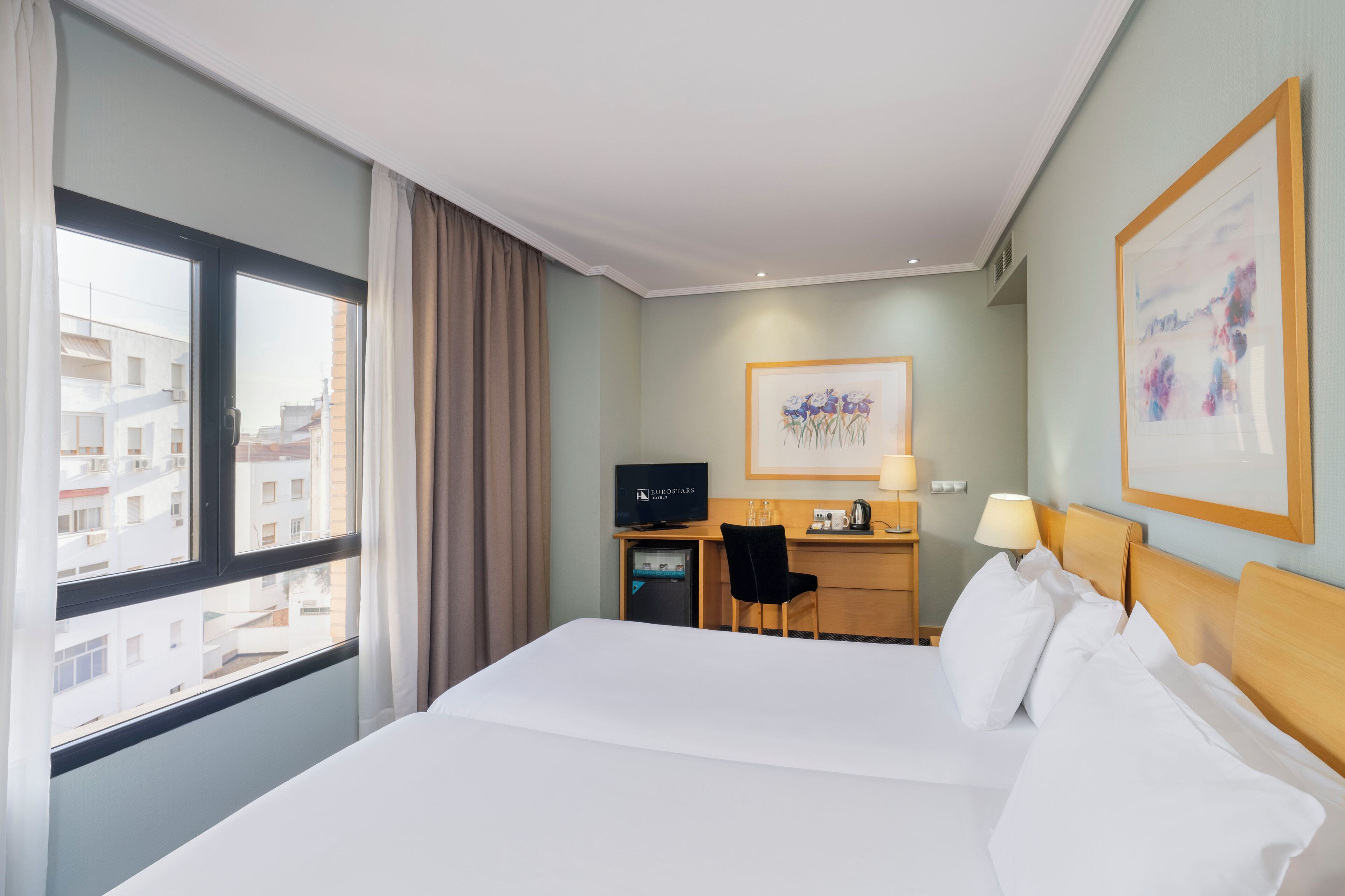 Habitación de hotel con una cama grande, un escritorio con computadora y una ventana con cortinas.