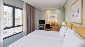 Habitación de hotel con una cama grande, un escritorio con computadora y una ventana con cortinas.