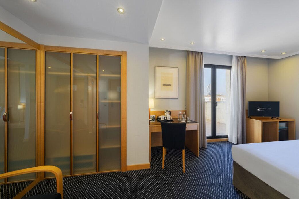 Una habitación de hotel con cama, escritorio, silla, televisor y armario.