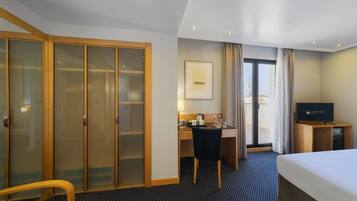 Una habitación de hotel con cama, escritorio, silla, televisor y armario.