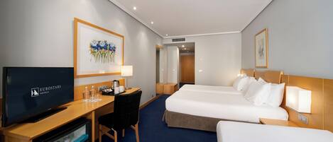 A hotel room with a TV, desk, two beds, and artwork on the walls.