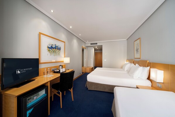 Una habitación de hotel con televisión, escritorio, dos camas y obras de arte en las paredes.