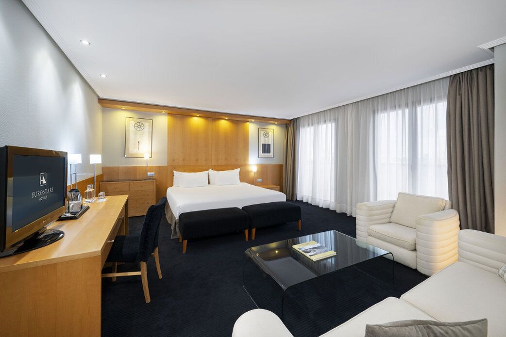 A hotel room with a bed, a desk with a computer, a sofa, and a coffee table.